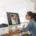 Una donna seduta alla scrivania, concentrata sul lavoro, con una stampante Xerox® C320 a colori Una donna seduta alla scrivania, concentrata sul lavoro, con una stampante Xerox® C320 a colori
